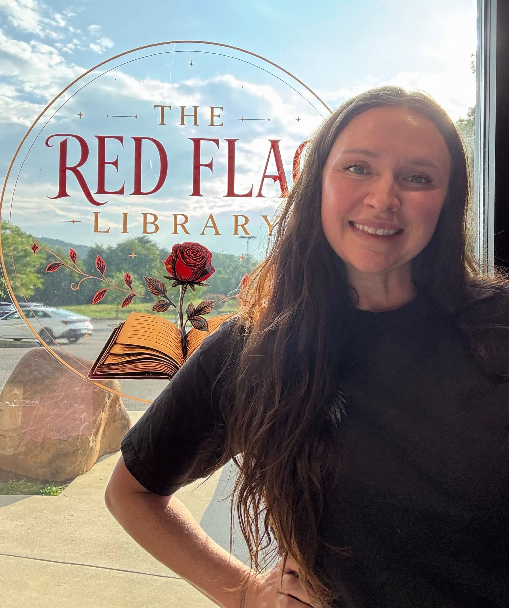Rachel, owner of The Red Flag Library, smiling in front of the storefront window